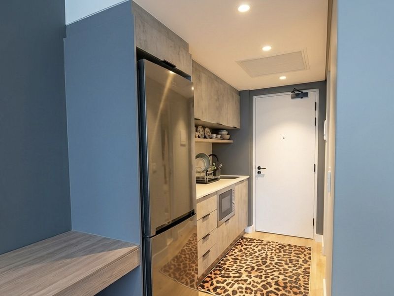 Compact modern kitchen featuring built-in cabinetry, integrated microwave, stainless steel refrigerator, and recessed lighting, conveniently located near the apartment entrance.