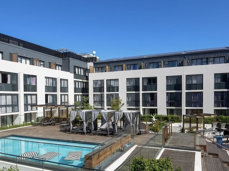 Modern apartment complex featuring a well-maintained swimming pool, timber decking, and shaded pergola areas within a landscaped courtyard setting.