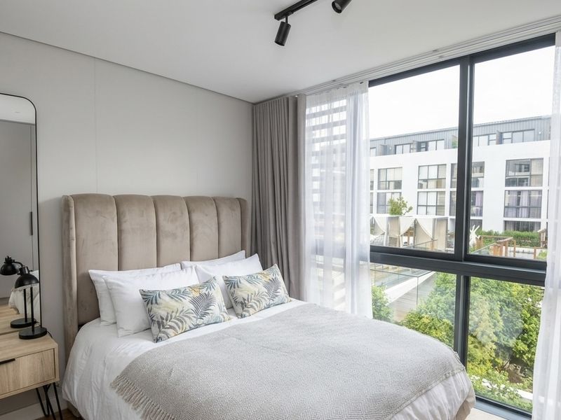 A modern, well-lit bedroom featuring large floor-to-ceiling windows, track lighting, and a built-in shelving unit with a contemporary aesthetic.