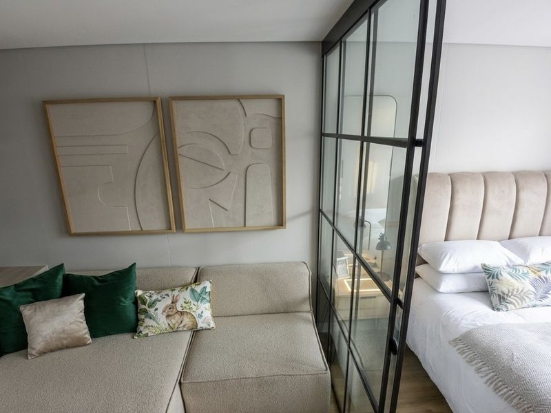 A modern bedroom featuring a stylish black metal-framed glass partition that separates the sleeping area from a cozy lounge space.