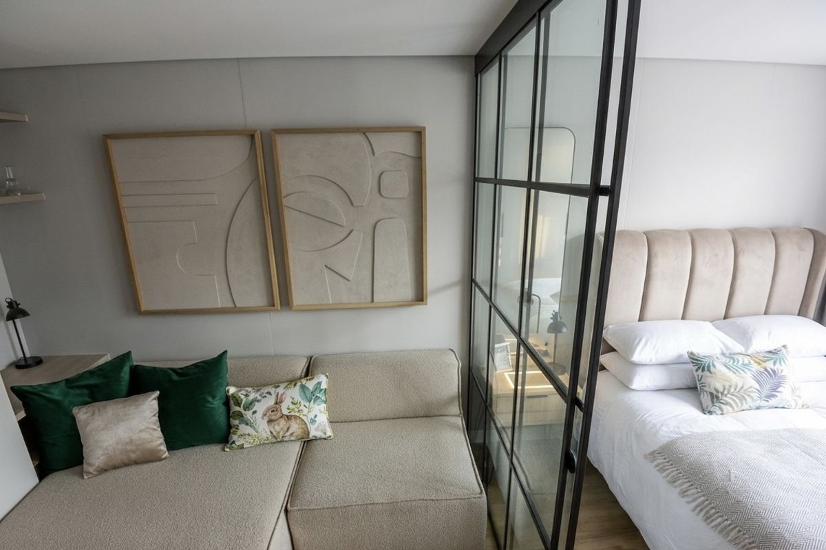 A modern bedroom featuring a stylish black metal-framed glass partition that separates the sleeping area from a cozy lounge space.