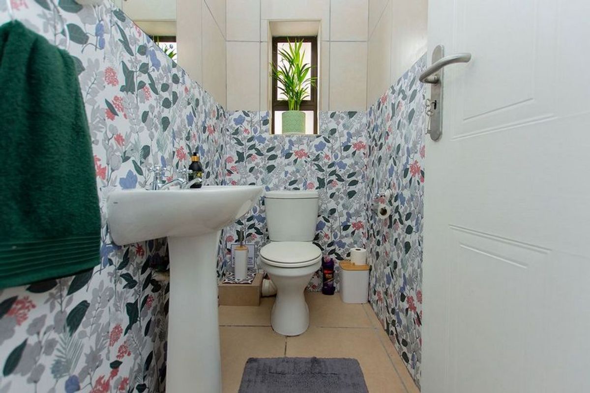 A compact bathroom featuring a pedestal sink, a standard toilet, and decorative floral-patterned wall tiling.