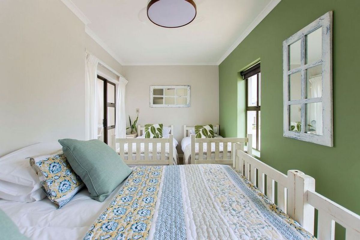 A bright bedroom featuring a green accent wall, large windows for natural light, and access to an outdoor balcony area.