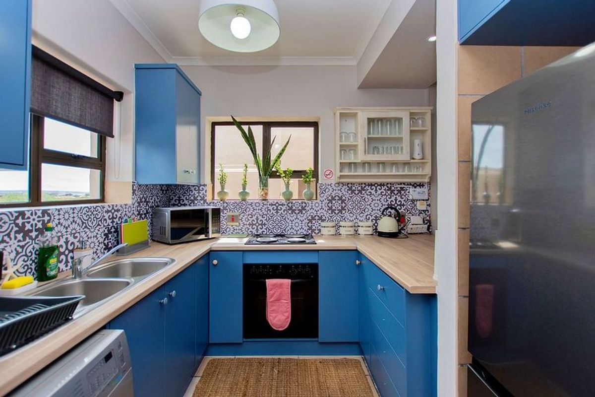 A compact, U-shaped kitchen featuring blue cabinetry, wood-look countertops, patterned tile backsplash, and integrated oven with hob.