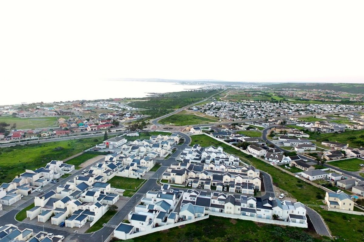 An aerial view of a residential townhouse complex situated in a coastal neighborhood with paved internal roads and surrounding green space.