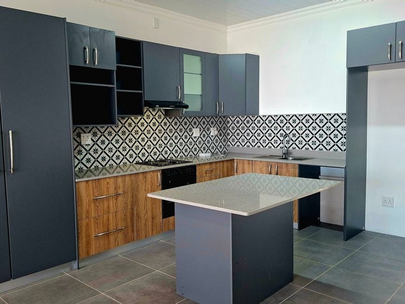 Modern kitchen featuring dark blue and wood-grain cabinetry, stone countertops, a central island, built-in hob, extractor fan, and stylish patterned backsplash tiling.