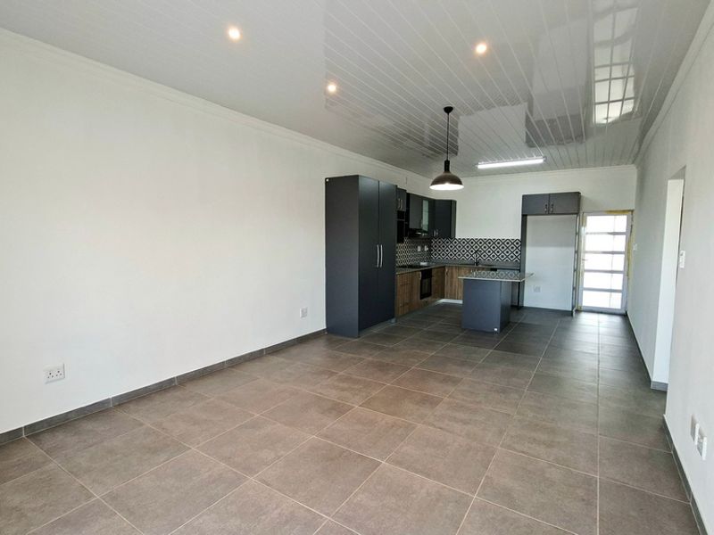 An open-plan living and kitchen area featuring modern cabinetry, a central island, tiled flooring, and a sleek glossy ceiling finish.