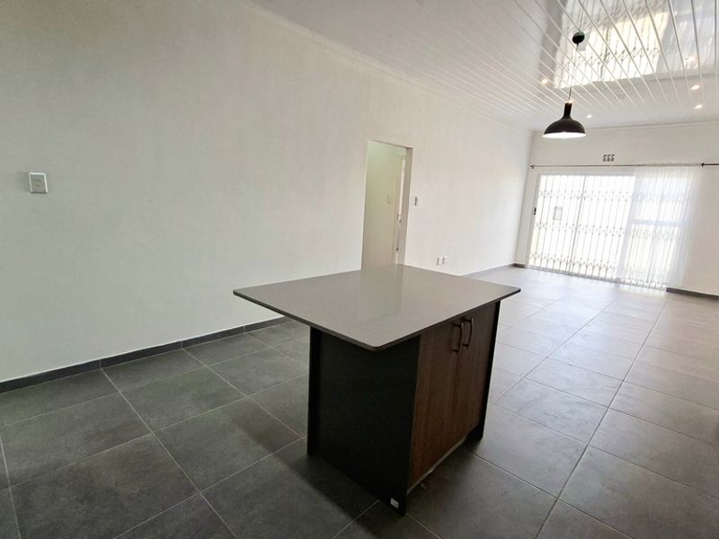 Spacious open-plan living and kitchen area featuring modern tiled flooring, a central kitchen island, and sliding doors leading to the exterior.