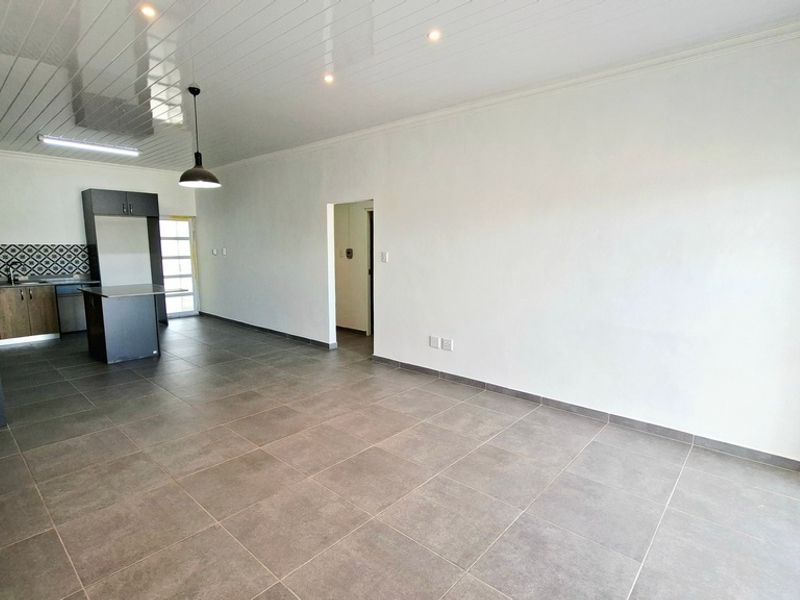 Spacious open-plan living and kitchen area featuring modern tiled flooring, contemporary cabinetry, a kitchen island, and clean, neutral finishes throughout.