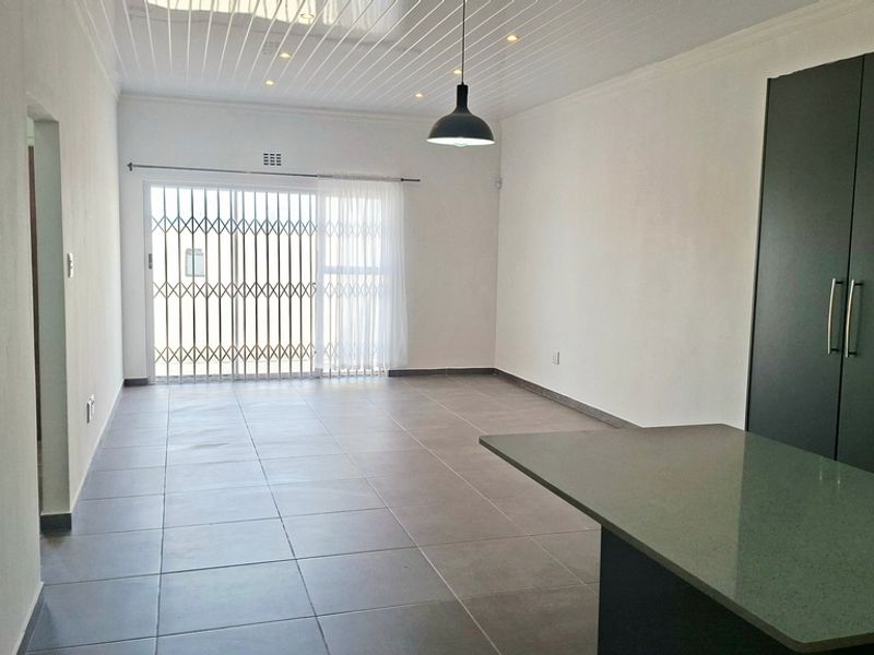 Spacious open-plan living area featuring modern tiled flooring, a sleek kitchen island with stone countertop, and a secure sliding door leading outdoors.