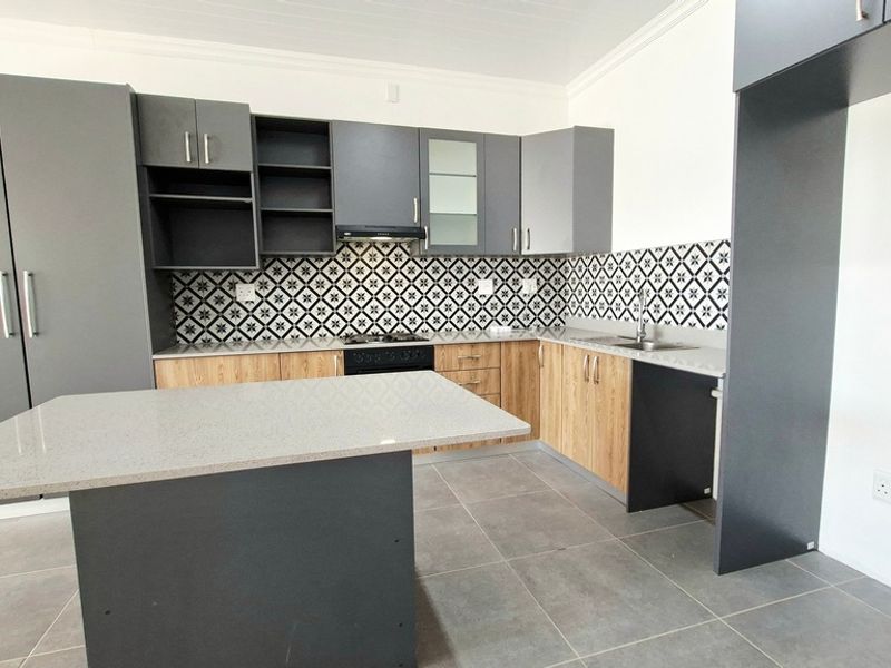 Modern kitchen featuring two-tone cabinetry, stone countertops, a central island, built-in oven, hob, extractor fan, and stylish patterned tiled backsplash.