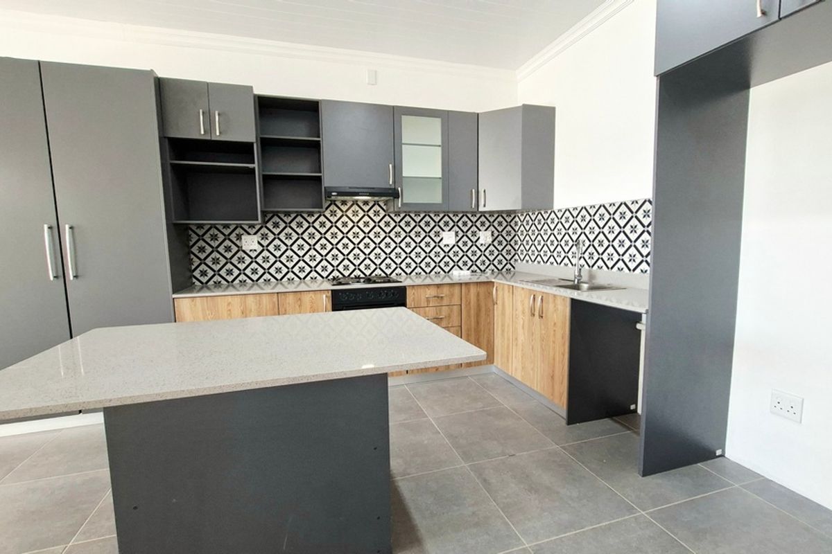 Modern kitchen featuring two-tone cabinetry, stone countertops, a central island, built-in oven, hob, extractor fan, and stylish patterned tiled backsplash.