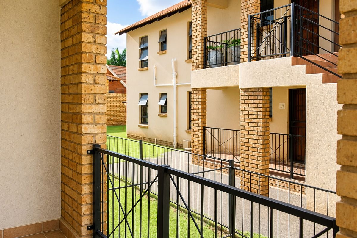 View of the apartment complex exterior featuring brick pillars, metal railings, and tiled balcony flooring.