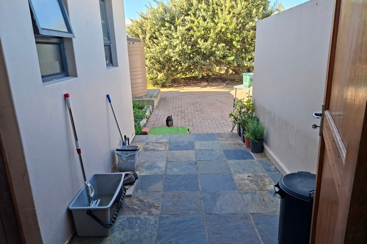 A rear exterior view showing a slate-tiled patio area leading to a paved garden space with a water tank.