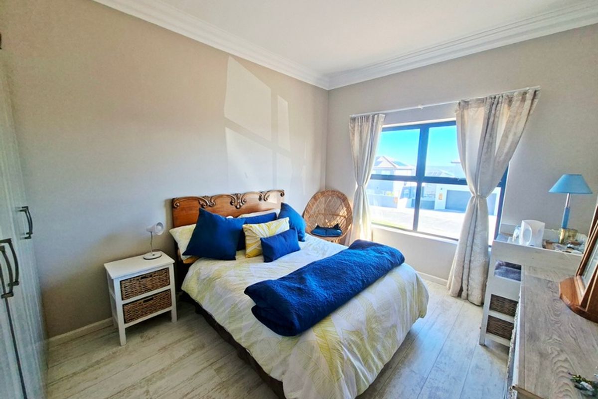A well-lit bedroom featuring laminate flooring, built-in wardrobe storage, and large aluminium-framed windows providing natural light.