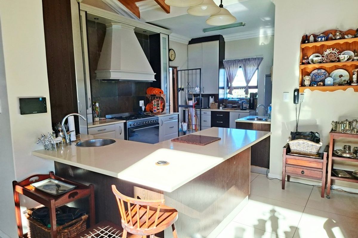Spacious kitchen featuring a central island with stone countertops, gas stove, extractor fan, and exposed timber ceiling beams, offering a functional layout.