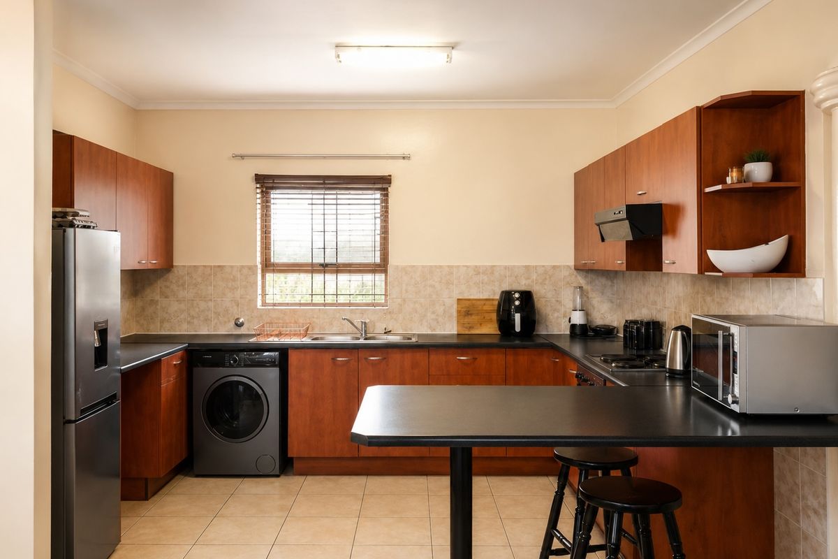 Functional kitchen featuring wood-tone cabinetry, dark laminate countertops, tiled backsplash, integrated appliances, and a convenient breakfast bar for casual dining.
