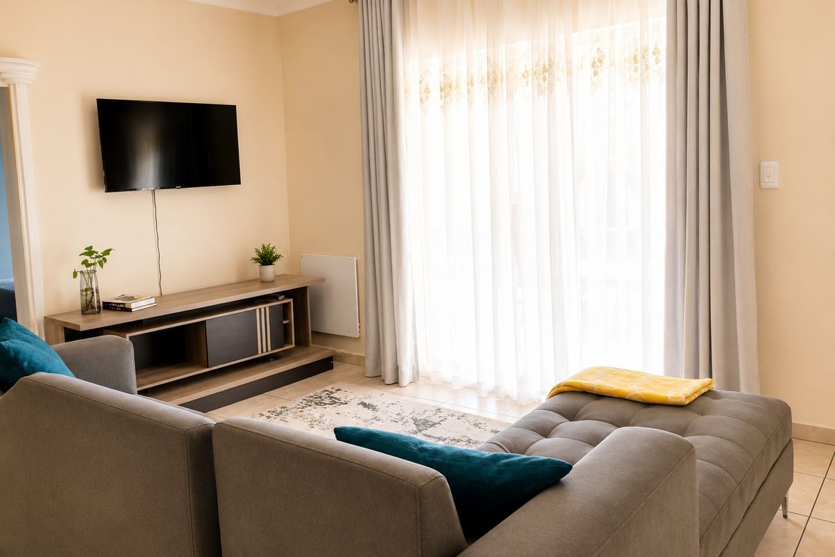 A well-maintained living room featuring tiled flooring, a wall-mounted heater, and large sliding glass doors with curtains providing natural light.