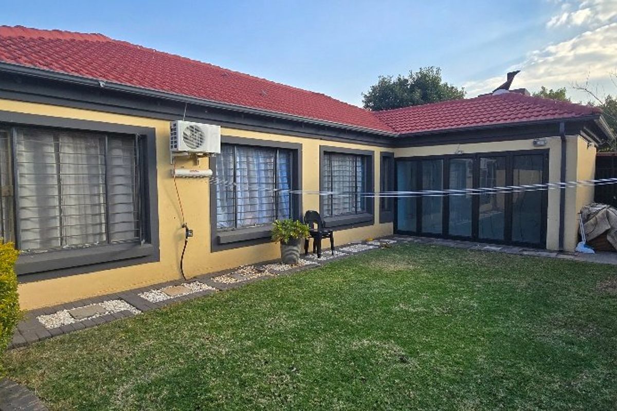 Rear view of the property featuring a lawn, paved border, red tiled roof, and black-framed sliding doors leading to the interior.