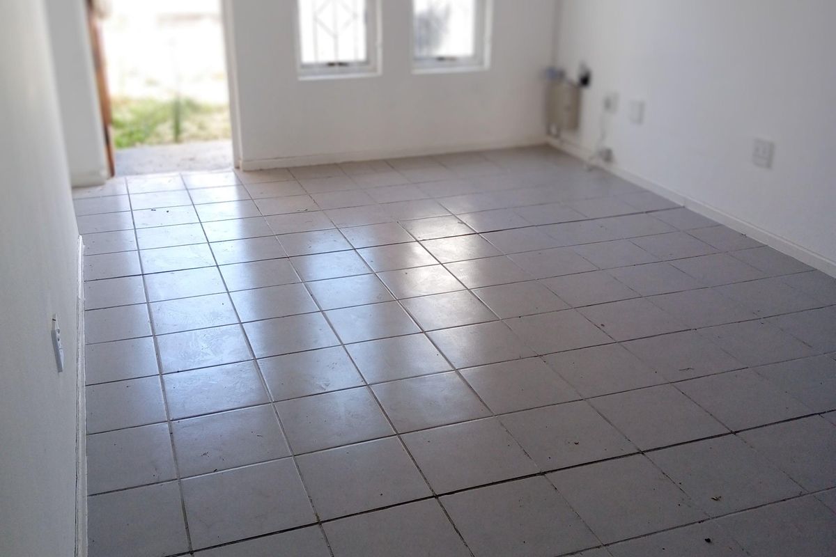 An empty living room featuring tiled flooring, security bars on the windows, and direct access to the exterior.
