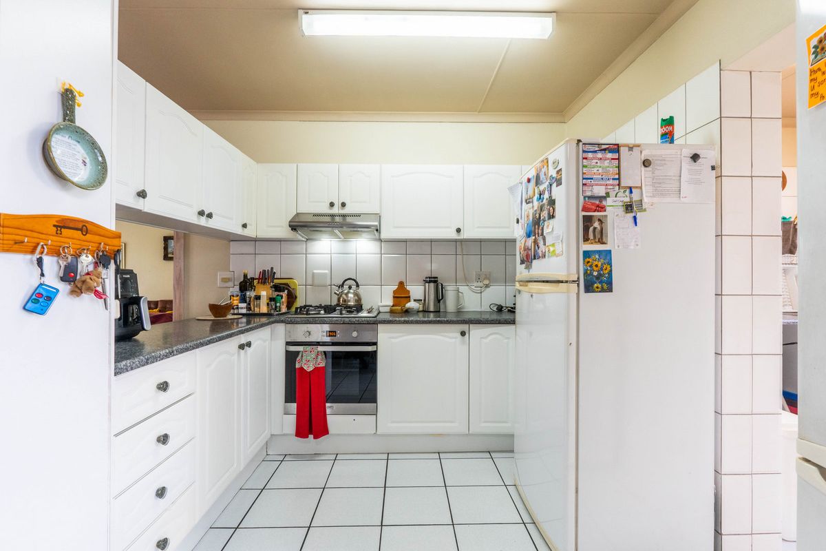 A functional kitchen featuring white cabinetry, granite-look countertops, a built-in oven with extractor fan, and tiled flooring.