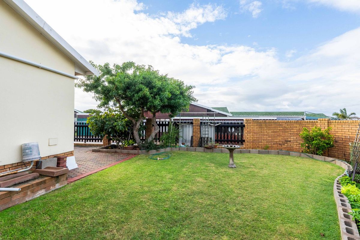 A private rear garden featuring a manicured lawn, paved patio area, and perimeter brick walling, providing a functional outdoor space for the townhouse.