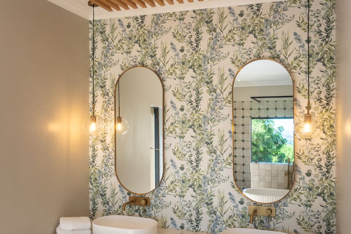 Modern bathroom featuring a double vanity with vessel sinks, stone countertop, decorative timber ceiling slats, and floral wallpaper.