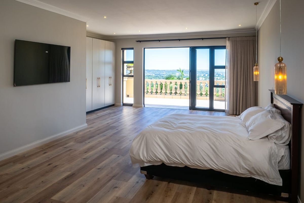 Spacious bedroom featuring modern wood-look flooring, built-in cabinetry, and large sliding glass doors opening onto a private balcony with scenic views.