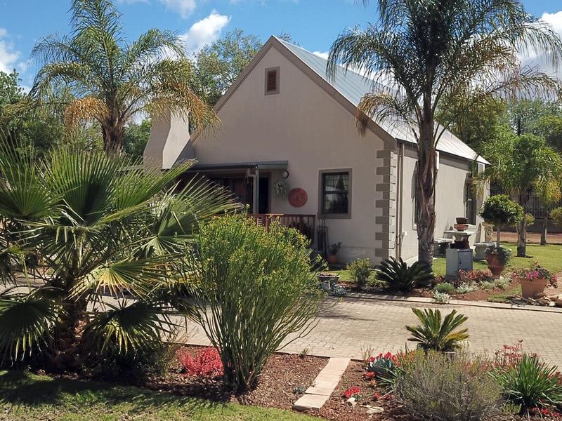 A charming single-story house featuring a pitched metal roof, a chimney, and a well-maintained front garden with a paved driveway.