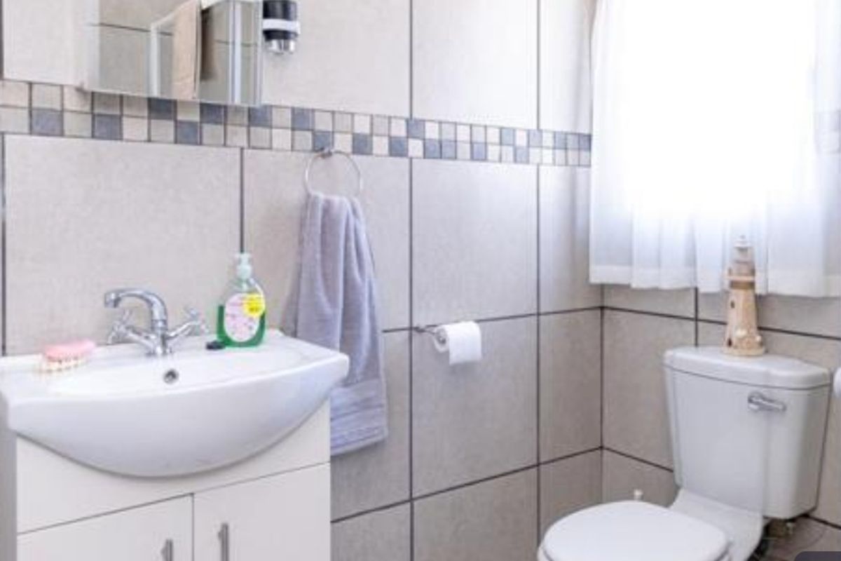 A functional bathroom featuring a vanity cabinet with a ceramic basin, wall-mounted mirror cabinet, and tiled walls with a decorative mosaic border.
