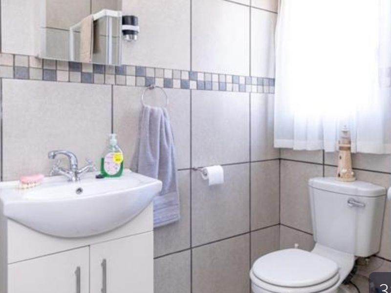 A functional bathroom featuring a vanity cabinet with a ceramic basin, wall-mounted mirror cabinet, and tiled walls with a decorative mosaic border.