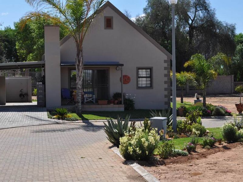 Front elevation of a well-maintained house featuring a paved driveway, attached carport, and established garden landscaping.