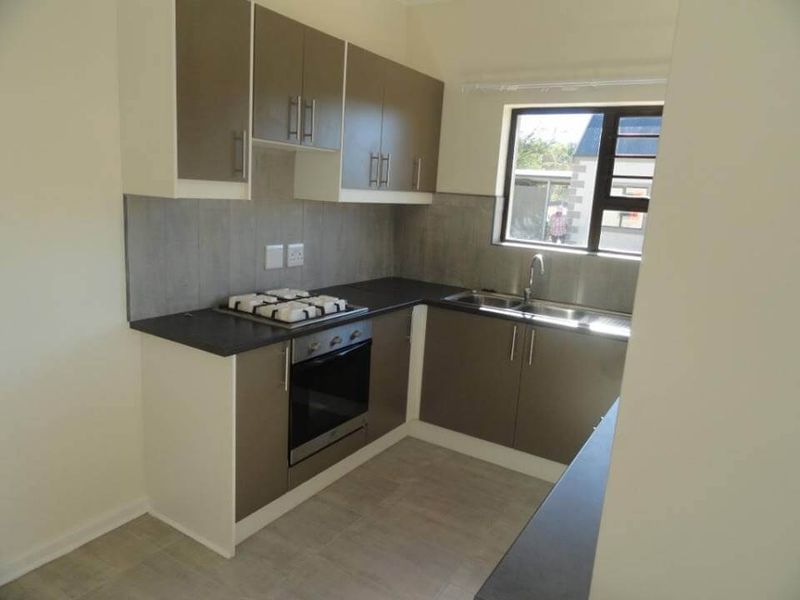A clean, modern kitchen featuring neutral-toned cabinetry, dark countertops, a built-in oven, gas hob, and a stainless steel sink with a window view.