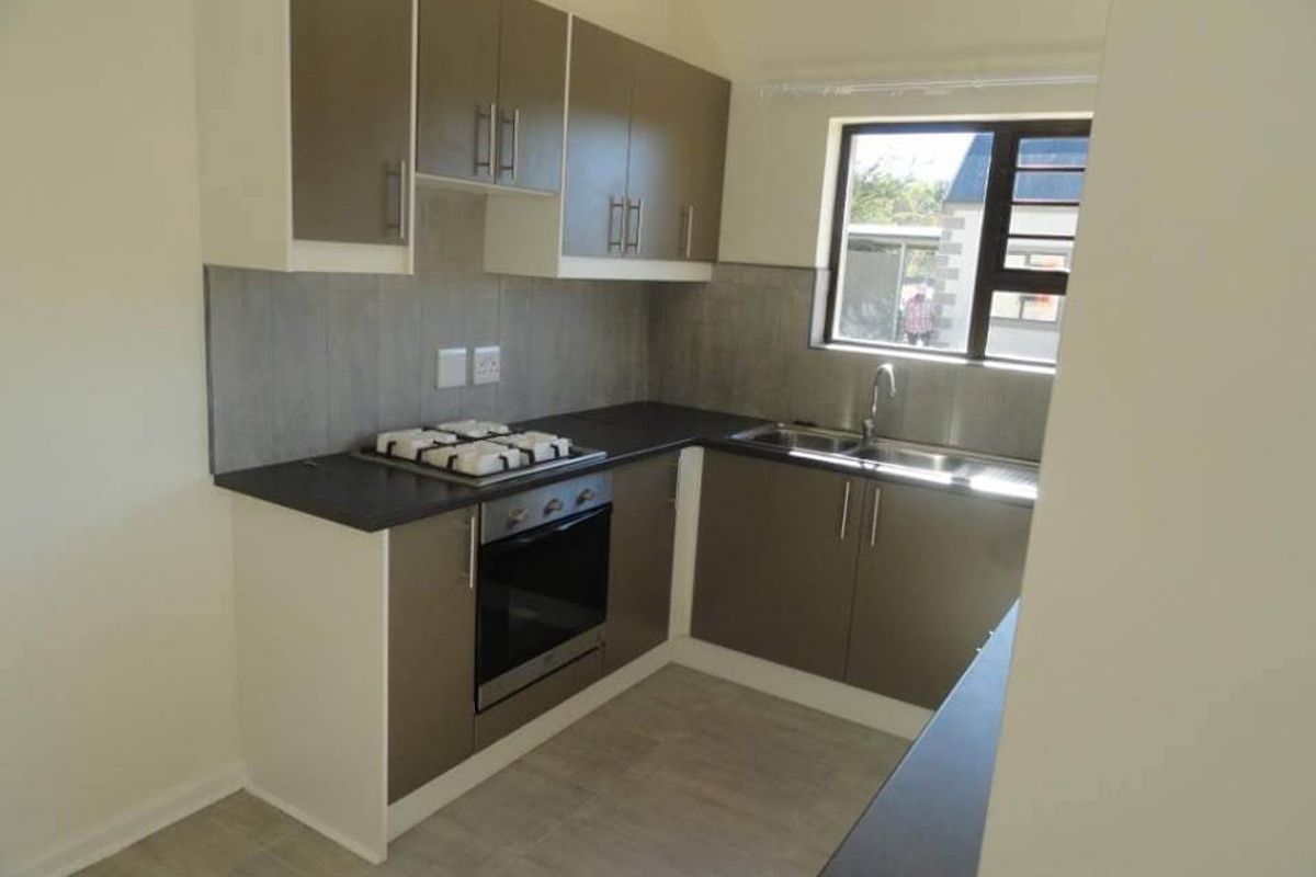 A clean, modern kitchen featuring neutral-toned cabinetry, dark countertops, a built-in oven, gas hob, and a stainless steel sink with a window view.