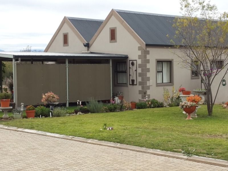 Front view of a single-story house featuring a dual-gabled roof, attached carport, and a well-maintained front lawn with paved driveway access.