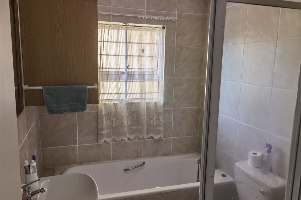 A functional bathroom featuring a bathtub, shower enclosure, toilet, and washbasin with neutral wall tiling and a built-in storage cabinet.
