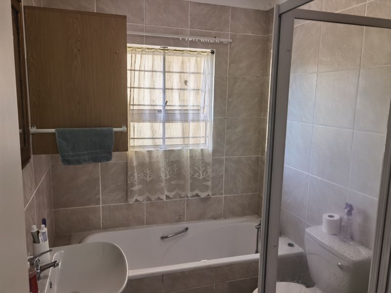 A functional bathroom featuring a bathtub, shower enclosure, toilet, and washbasin with neutral wall tiling and a built-in storage cabinet.