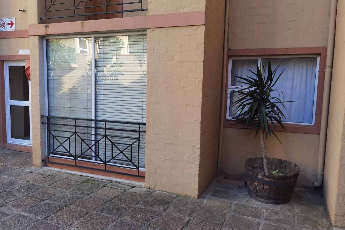 Ground floor apartment exterior featuring a paved patio area, sliding glass door access, and metal balustrades against a brick facade.