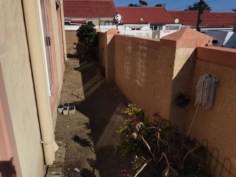 A narrow rear exterior side passage featuring a boundary wall and unlandscaped ground area.