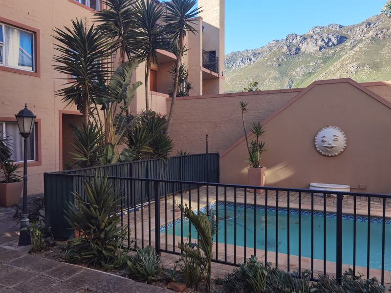 Outdoor pool area featuring a fenced swimming pool, paved surround, and mountain views, set within a residential apartment complex courtyard.