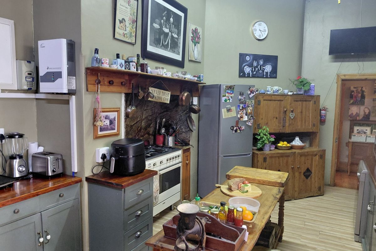 A rustic-style kitchen featuring wooden cabinetry, stone splashback, gas stove, and a central wooden island, with a wall-mounted solar inverter.