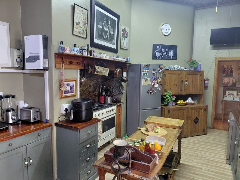 A rustic-style kitchen featuring wooden cabinetry, stone splashback, gas stove, and a central wooden island, with a wall-mounted solar inverter.