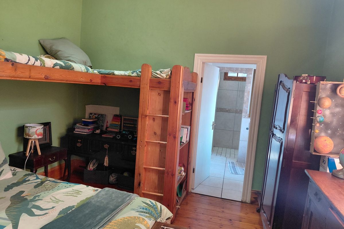 A bedroom featuring original timber flooring and green painted walls, with an adjoining en-suite bathroom visible through the doorway.