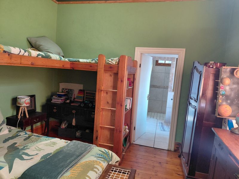 A bedroom featuring original timber flooring and green painted walls, with an adjoining en-suite bathroom visible through the doorway.