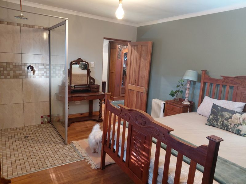 A bedroom featuring an open-plan walk-in shower with glass enclosure, timber flooring, and a solid wood door leading to an adjacent space.