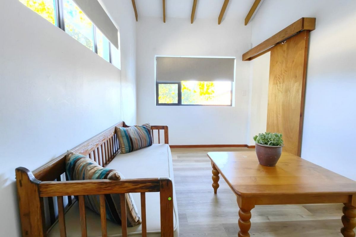 A bright living room featuring exposed timber ceiling beams, light laminate flooring, and a sliding timber barn door.