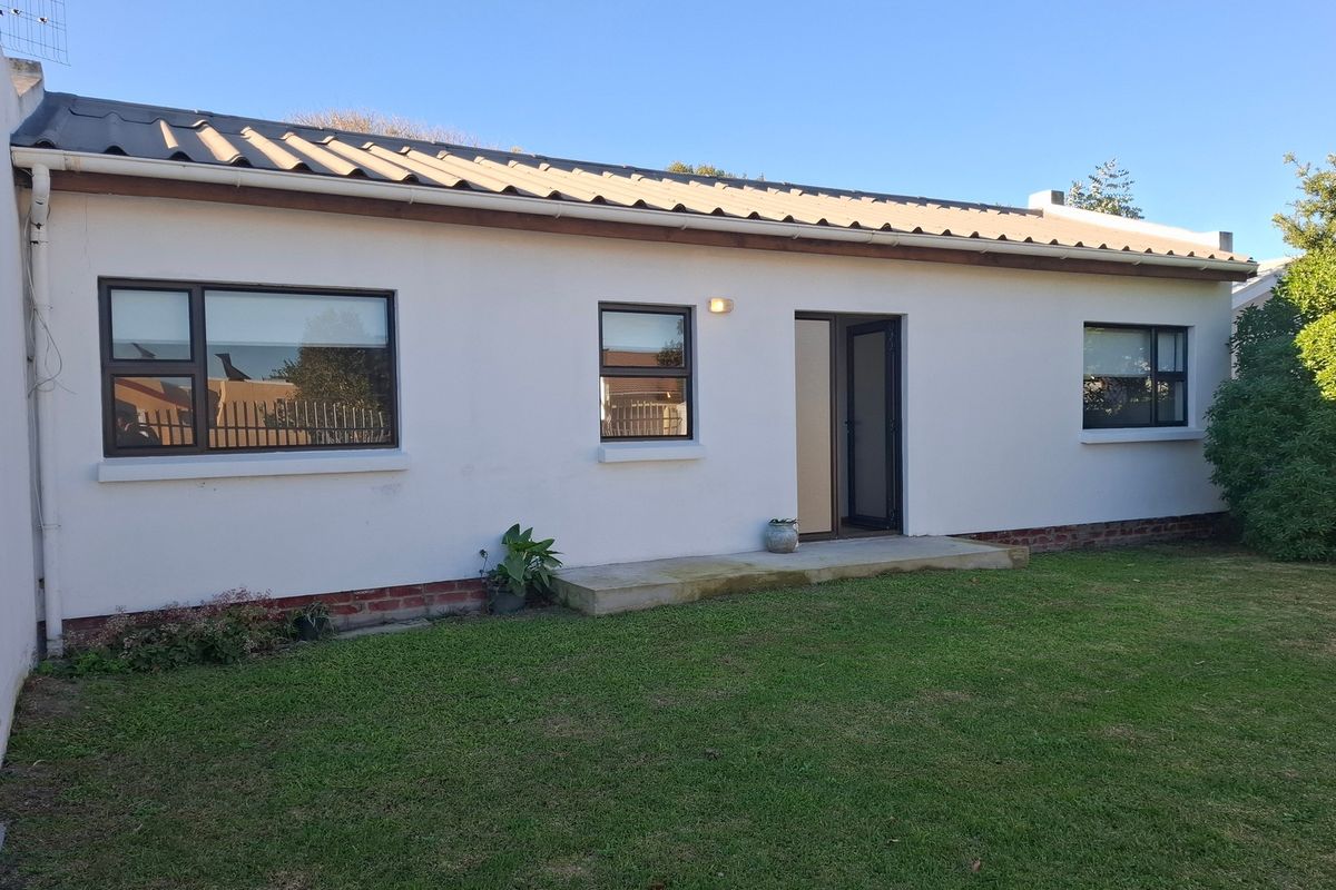 Rear exterior view of the house featuring a corrugated metal roof, white rendered walls, and aluminium-framed windows overlooking a lawn.