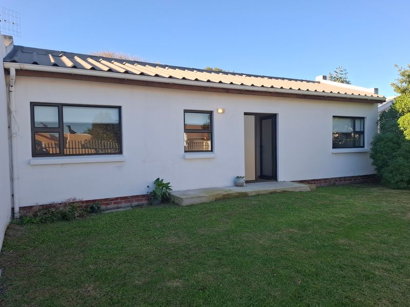 Rear exterior view of the house featuring a corrugated metal roof, white rendered walls, and aluminium-framed windows overlooking a lawn.