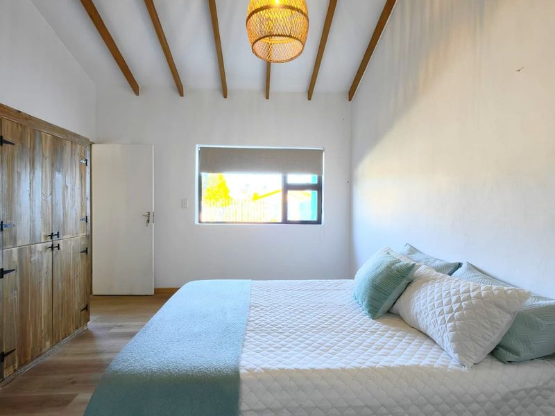 A bright bedroom featuring exposed timber ceiling beams, laminate flooring, and a built-in wooden wardrobe, creating a warm and inviting atmosphere.