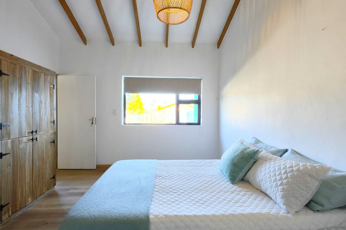 A bright bedroom featuring exposed timber ceiling beams, laminate flooring, and a built-in wooden wardrobe, creating a warm and inviting atmosphere.